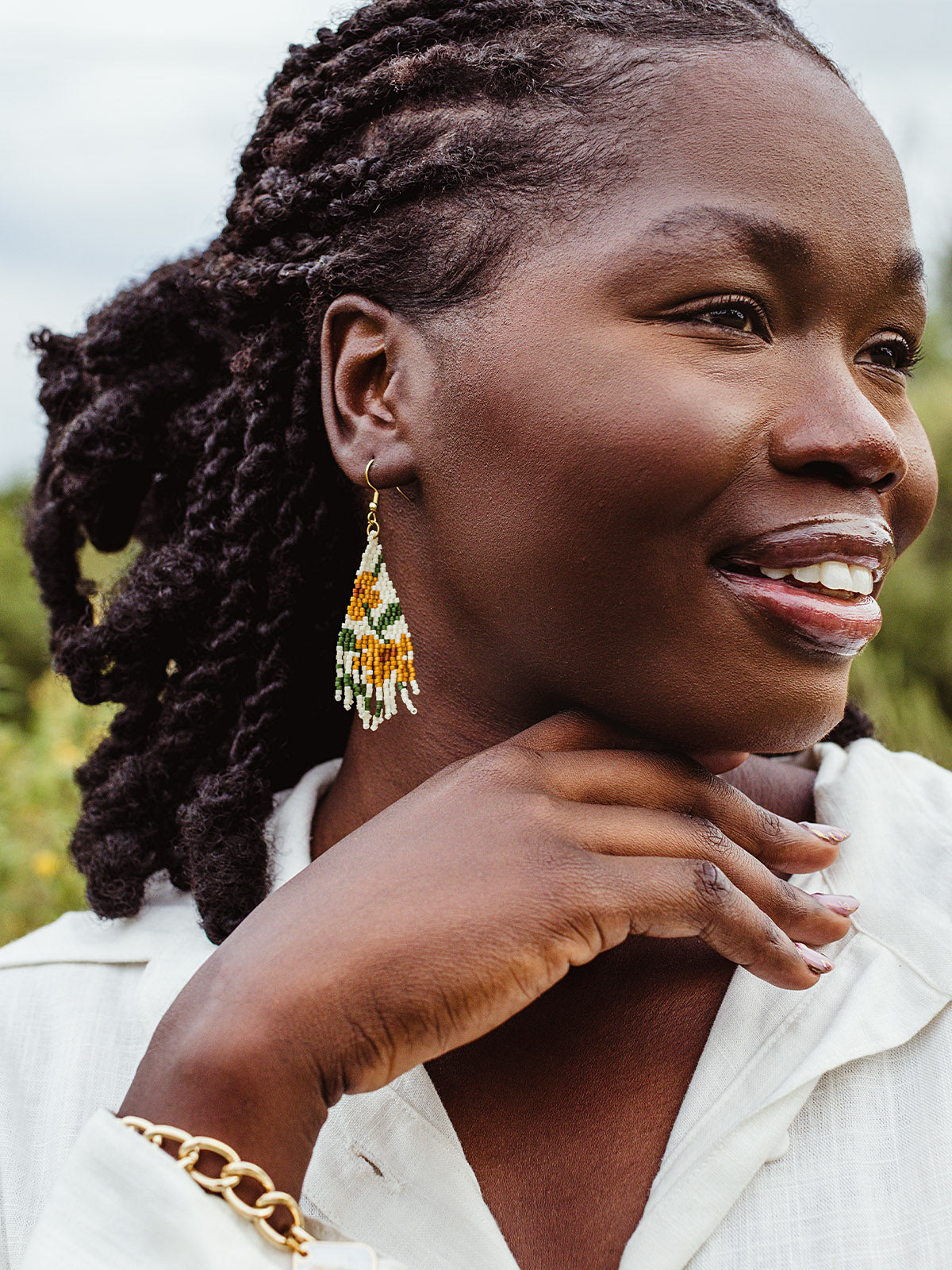 Woman smiling in handmade beaded fringe earrings with yellow, green, and white pattern, ethical fair trade jewelry.