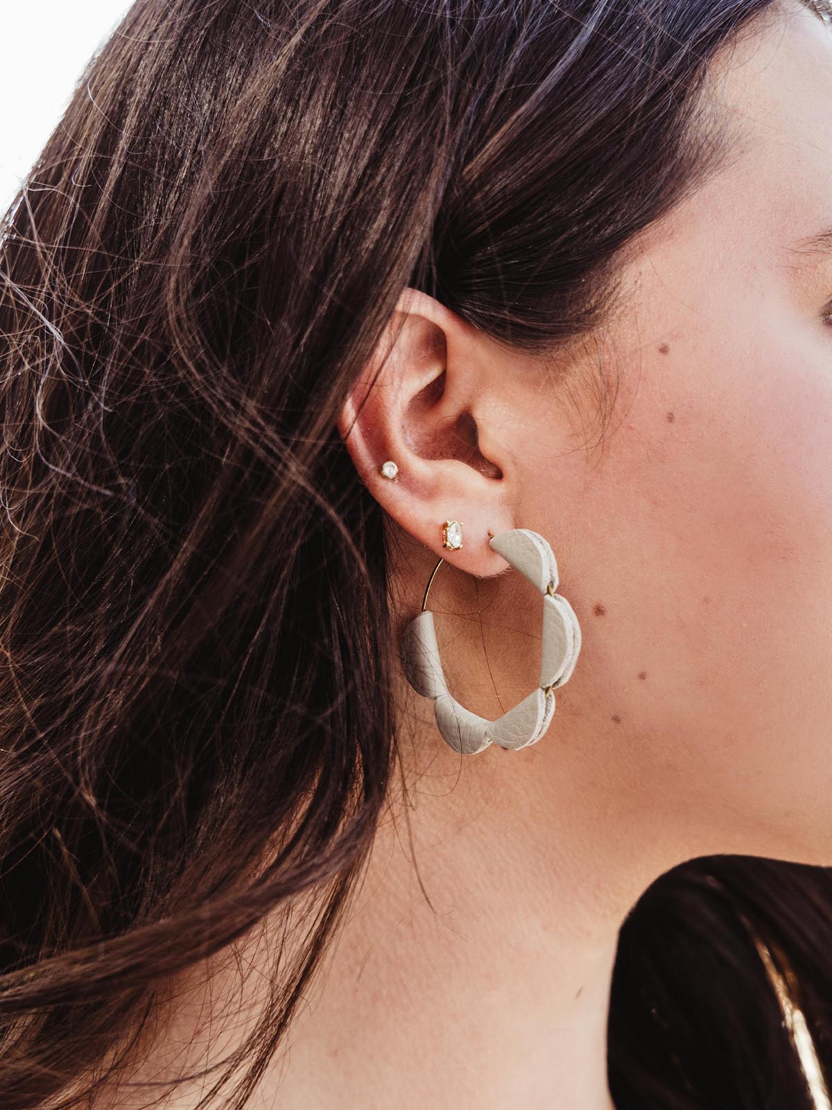 Side profile of a woman wearing handcrafted white leather hoop earrings with a semi-circle design, paired with other delicate earrings.
