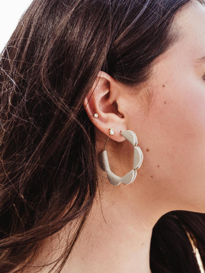 Side profile of a woman wearing handcrafted white leather hoop earrings with a semi-circle design, paired with other delicate earrings.