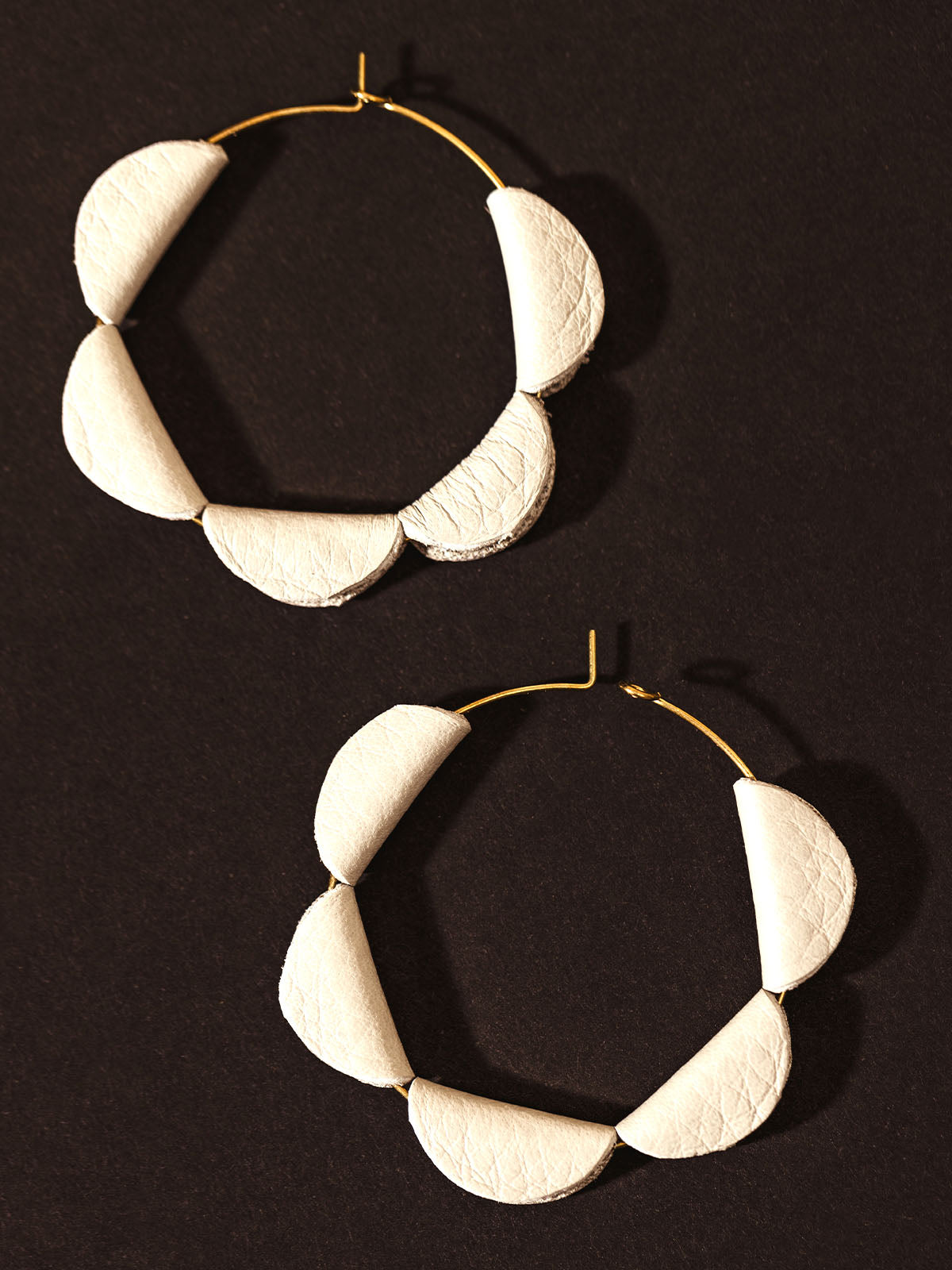 Close-up of handcrafted white leather hoop earrings with a unique semi-circle design, displayed on a dark background.
