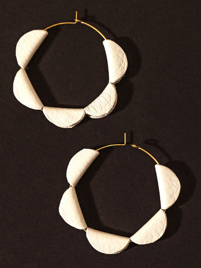 Close-up of handcrafted white leather hoop earrings with a unique semi-circle design, displayed on a dark background.