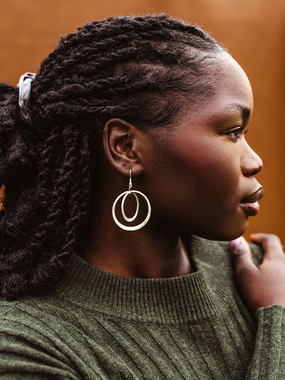Side view of woman wearing large silver double hoop earrings, modern handmade statement jewelry with braided hairstyle.