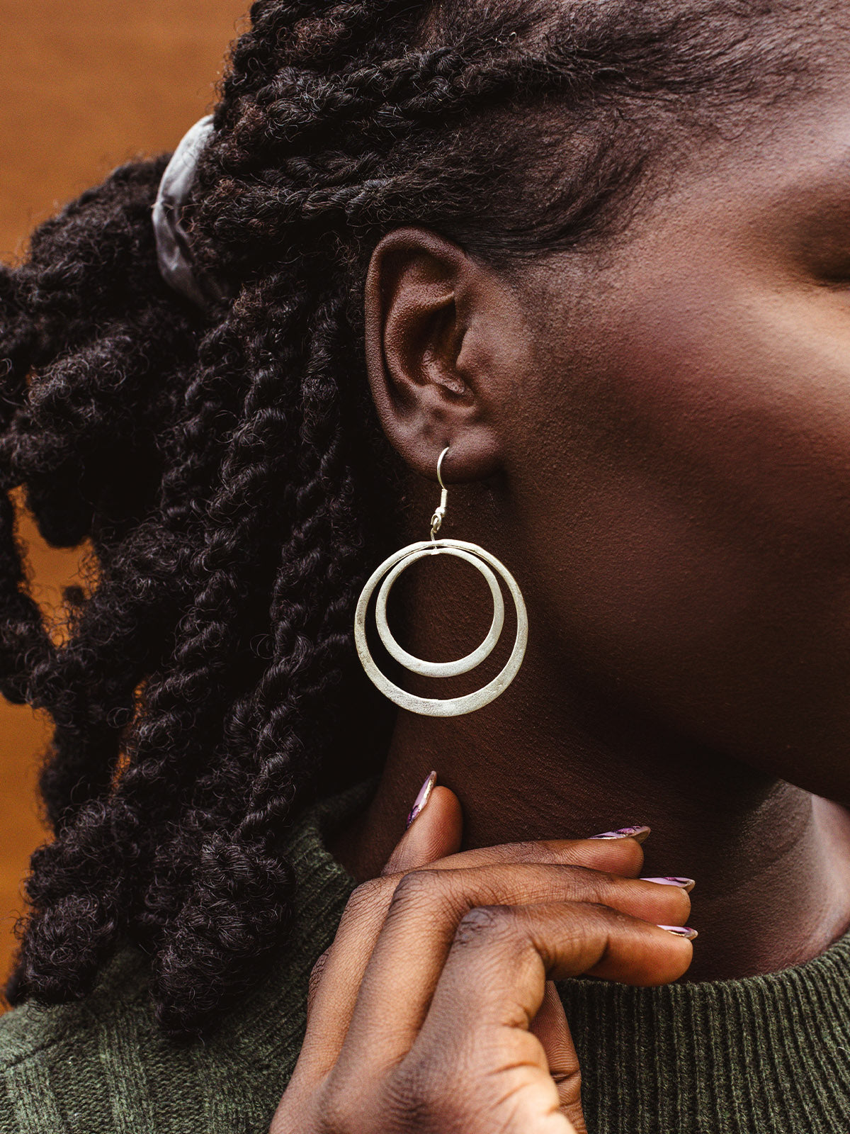 Close-up of silver double hoop earrings styled with green knit sweater, ethical handmade statement jewelry.