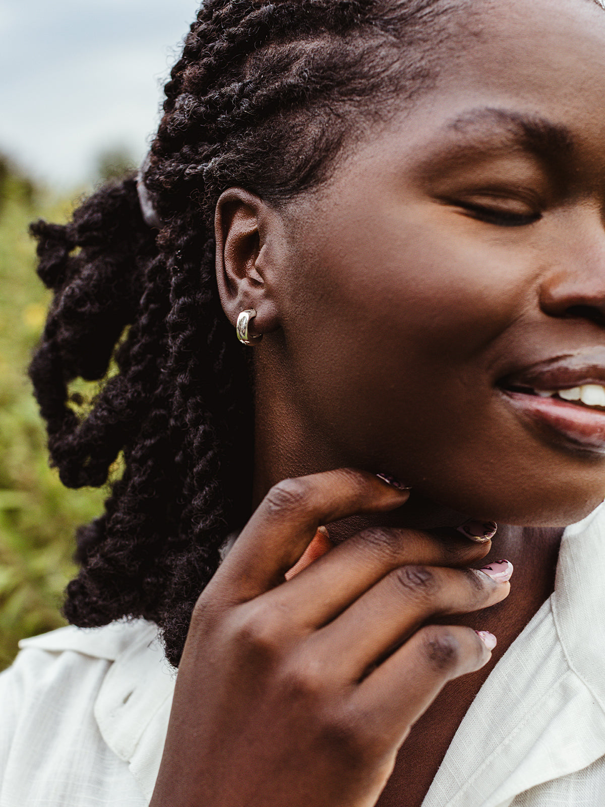 Close-up of woman smiling in silver chunky hoop earrings, ethical handmade jewelry styled with white button-up shirt.