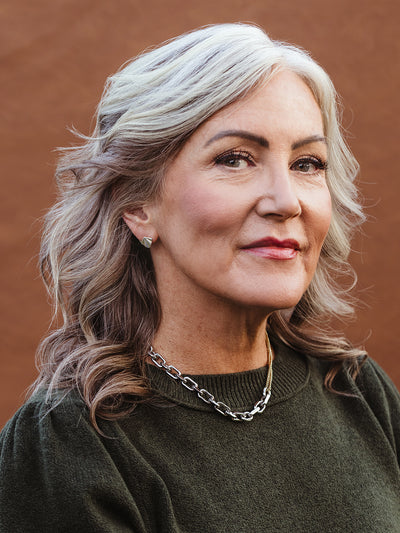 Woman with silver hair wearing geometric stud earrings and chunky chain necklace, elegant handcrafted jewelry for everyday sustainable style.