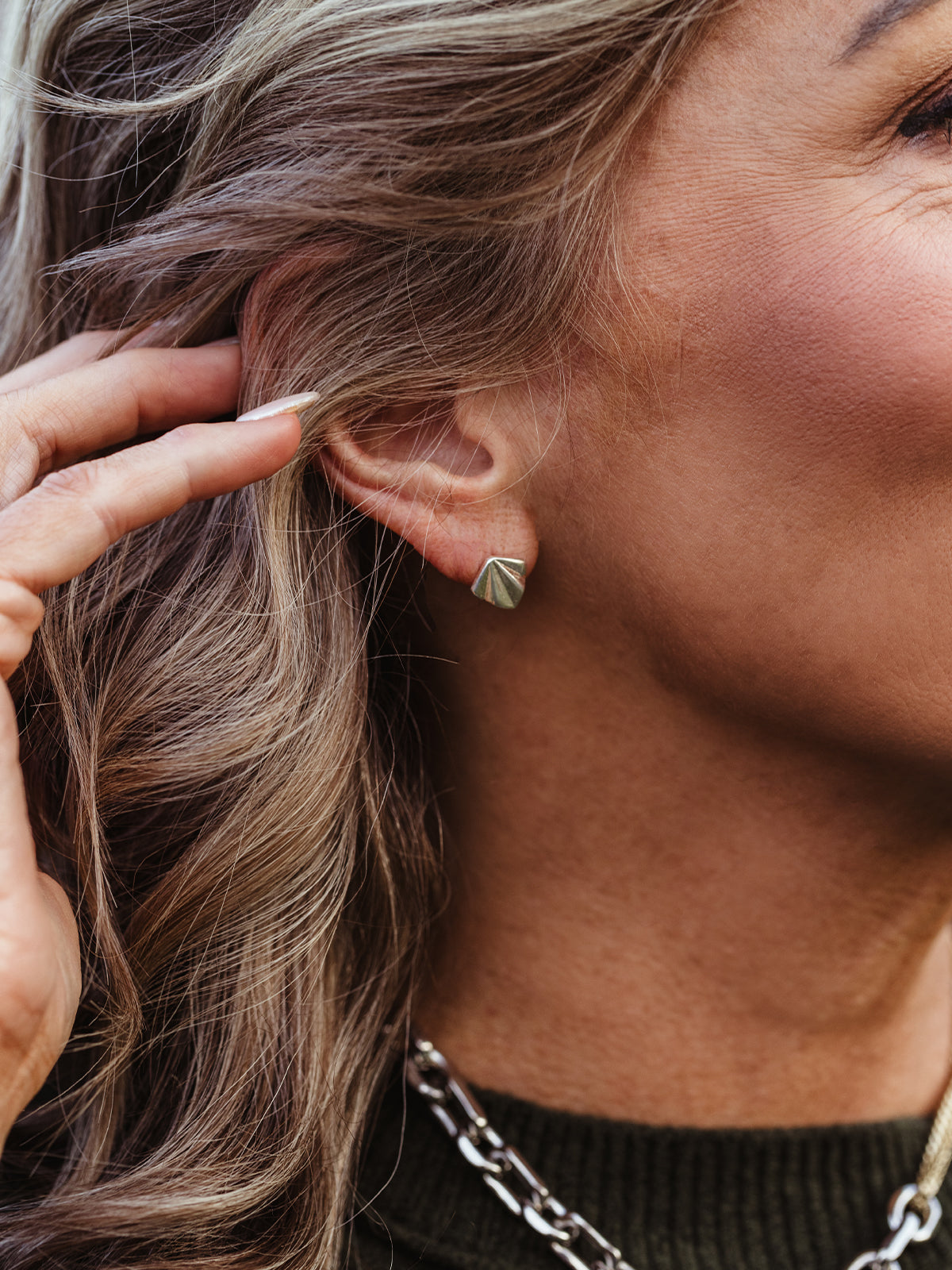 Close-up of silver geometric stud earrings on woman with wavy hair, minimalist artisan-made jewelry designed for timeless wear.