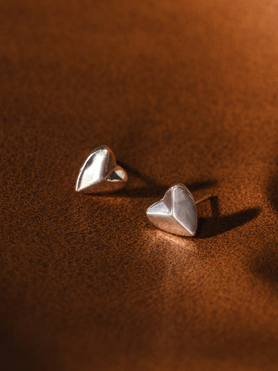 Sterling silver heart stud earrings on warm brown background – minimalist ethical jewelry for everyday wear.