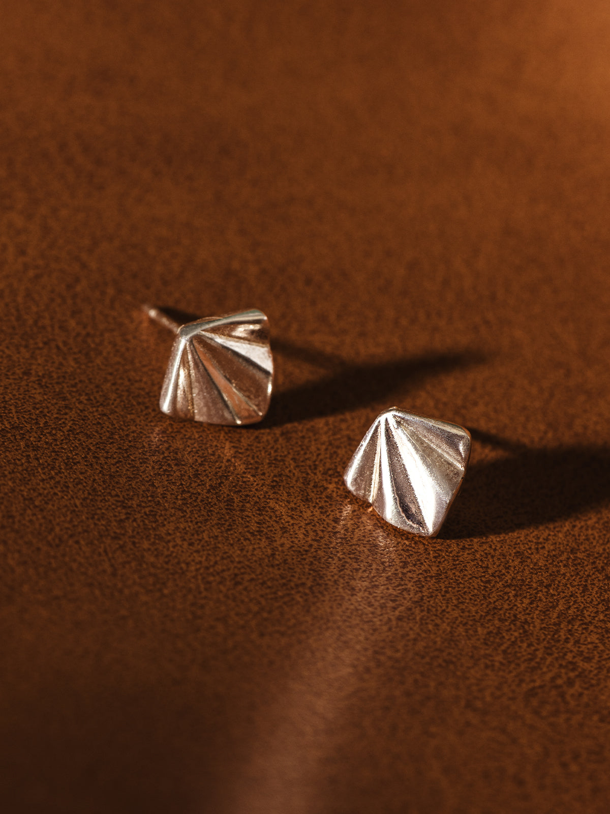 Textured sterling silver fan-shaped stud earrings on brown backdrop – modern handcrafted ethical jewelry.