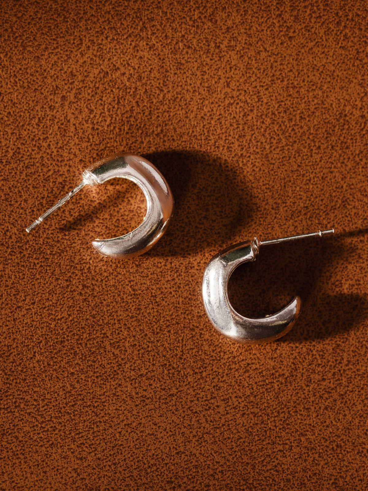 Pair of sterling silver crescent hoop earrings displayed on brown background – handcrafted ethical jewelry for women.