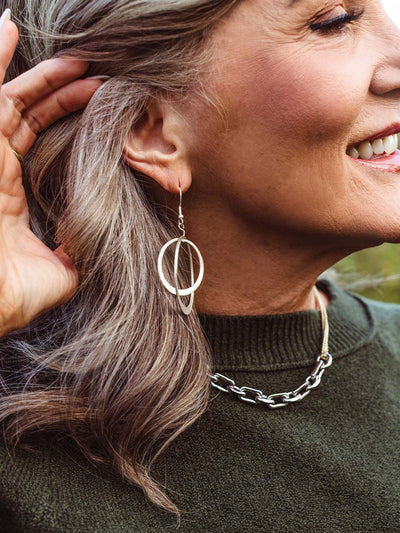 Close-up of woman adjusting hair to show artisan-made silver double hoop earrings paired with a modern chain necklace — fair trade sustainable jewelry.