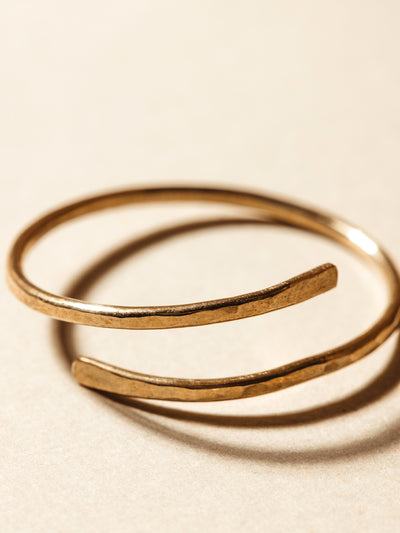 Close up of gold hammered wrap ring on cream background.