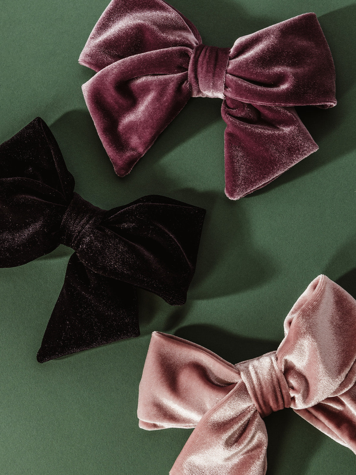 Set of three oversized velvet hair bows in mauve, black, and blush displayed on green background – elegant handmade accessories for women and girls.
