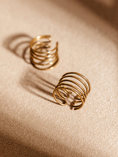 Set of two handcrafted brass coil rings with an open adjustable design on a soft tan surface. Fair trade minimalist jewelry for everyday wear.