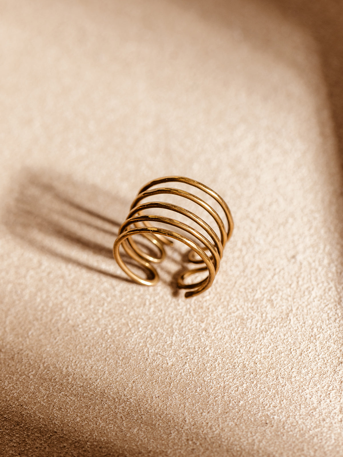 Handmade brass wrap ring with five open coil bands resting on a warm neutral background. Adjustable minimalist ring ethically crafted by artisans.