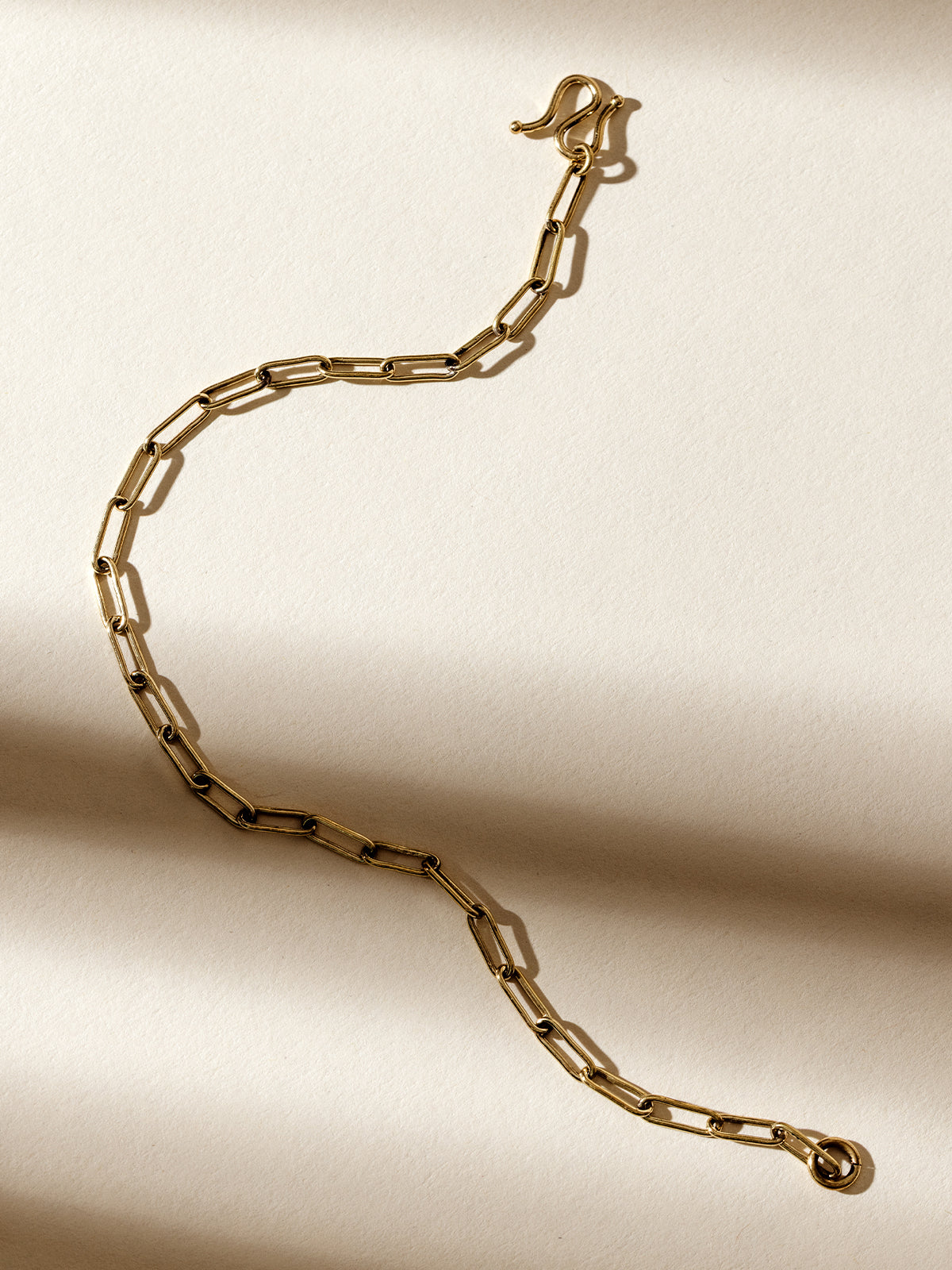 Gold chain link bracelet with a hook clasp, photographed on a textured cream background with soft natural shadows, highlighting its minimalist and elegant design.