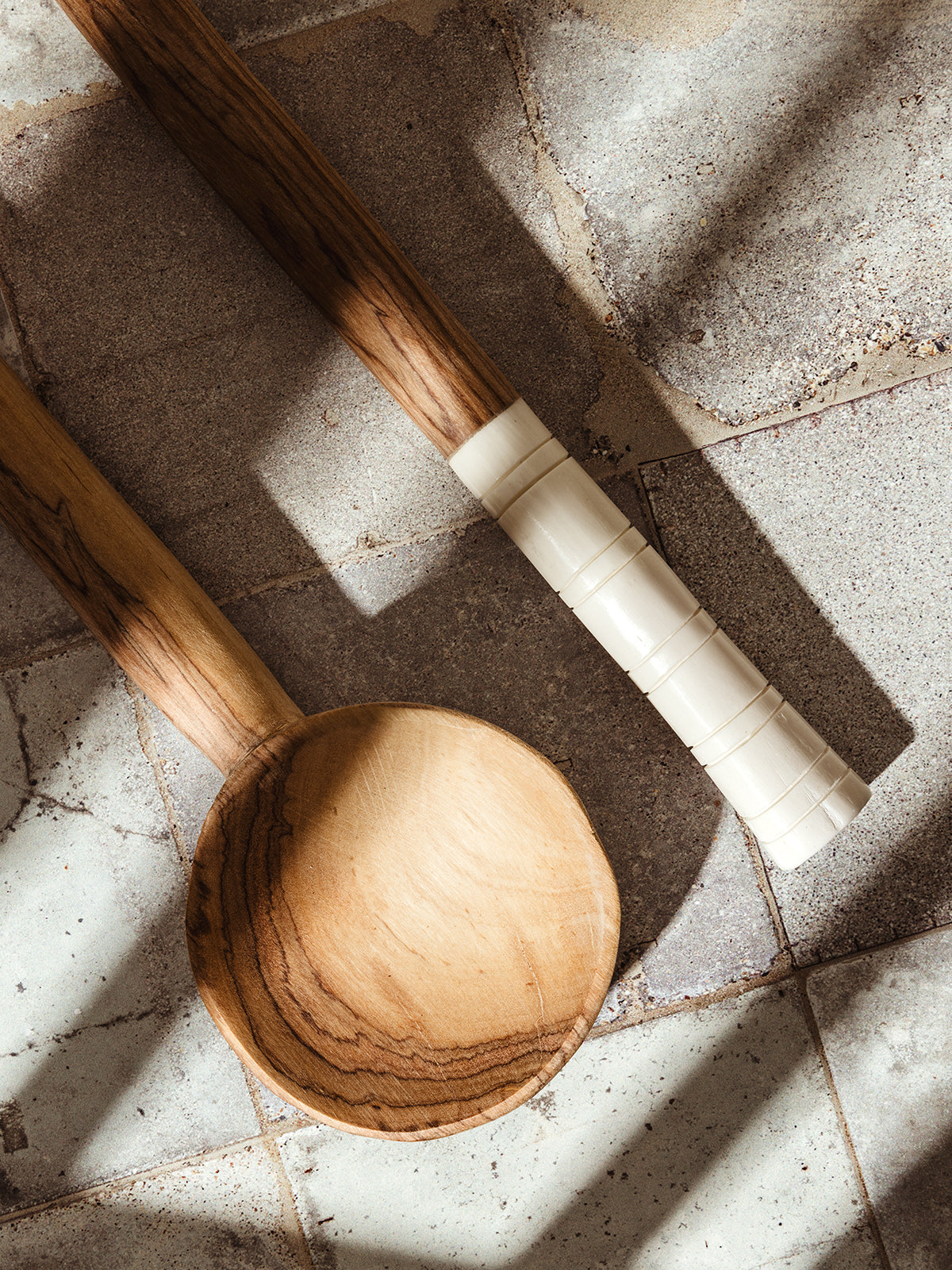 Close-up of a handcrafted wooden spoon with smooth grain and carved white handle, displayed on a weathered tile surface.