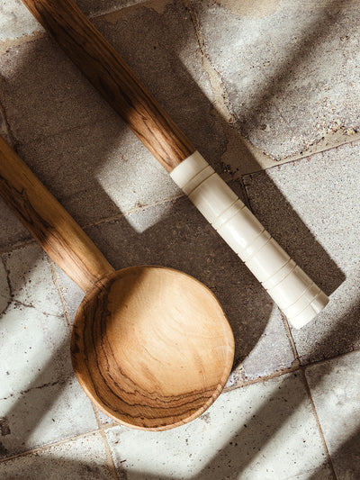 Close-up of a handcrafted wooden spoon with smooth grain and carved white handle, displayed on a weathered tile surface.