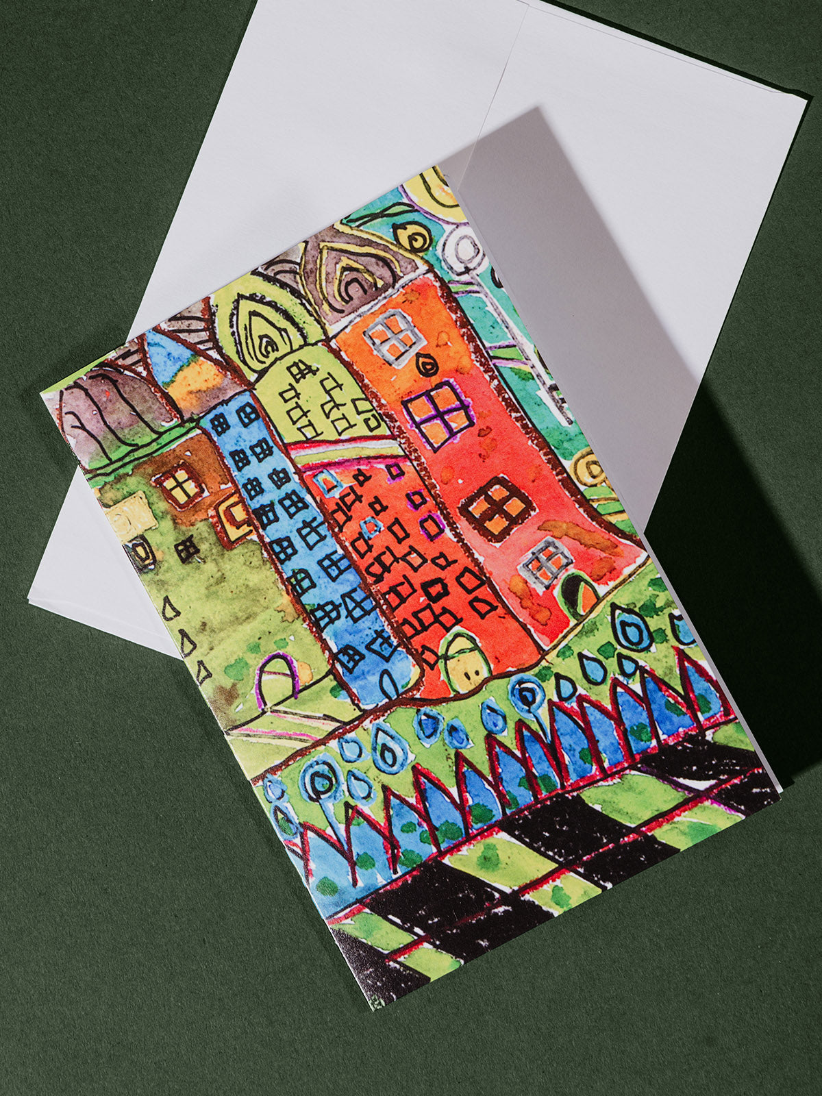 A vertically oriented greeting card on a white envelope featuring a bright, abstract drawing of tall, colorful buildings with whimsical windows and details.