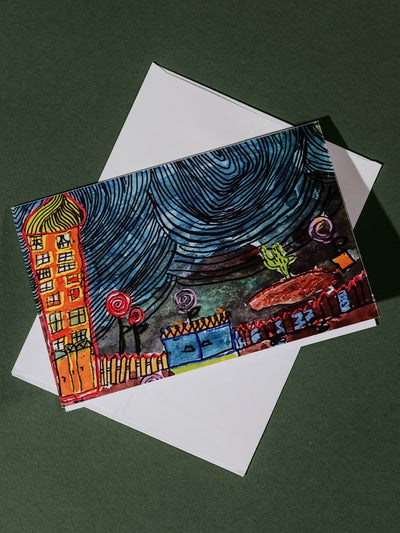A greeting card on a white envelope showcasing a playful, childlike drawing of a starry night sky over whimsical homes and swirling patterns.