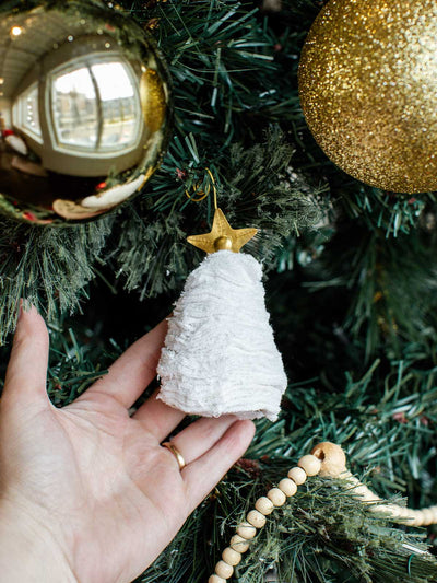 Hand holding a handmade white Christmas tree ornament with a gold star topper, hung on a decorated Christmas tree with gold baubles.