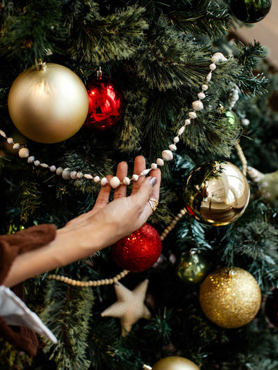 Close-up of hand styling eco-friendly paper bead garland among colorful Christmas ornaments on a holiday tree.