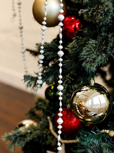 Sustainable paper bead garlands draped on a decorated Christmas tree with gold, red, and green ornaments for eco-friendly holiday decor.