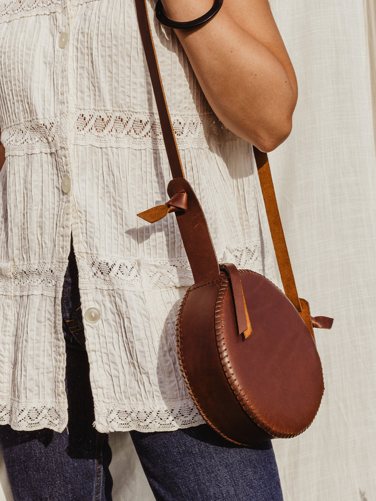 Female model with canteen purse over the shoulder In front of white fabric backdrop. 