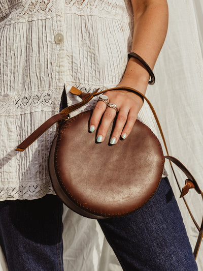 Female model clutching the canteen purse with her hand agains a fabric white backdrop.