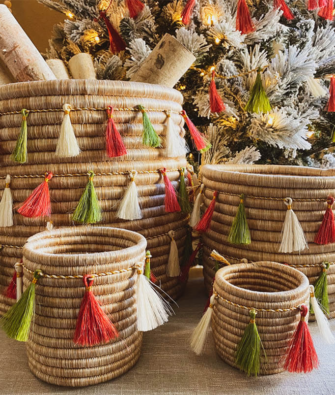 4 handwoven baskets of different sizes with red green and white tassel garlands in front of a Christmas Tree
