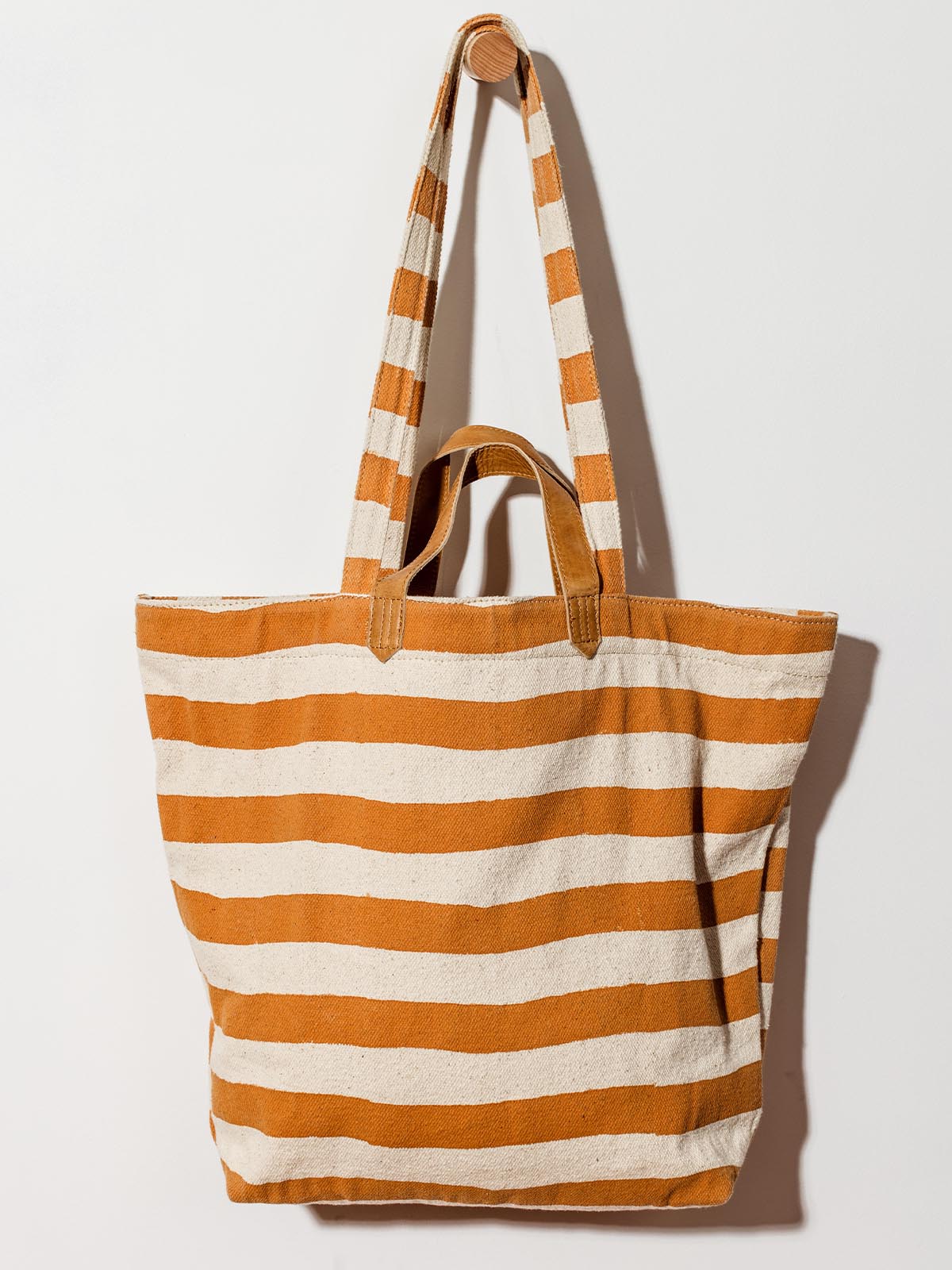 Carryall canvas tote with cream and orange stripes on white wall hanging. 