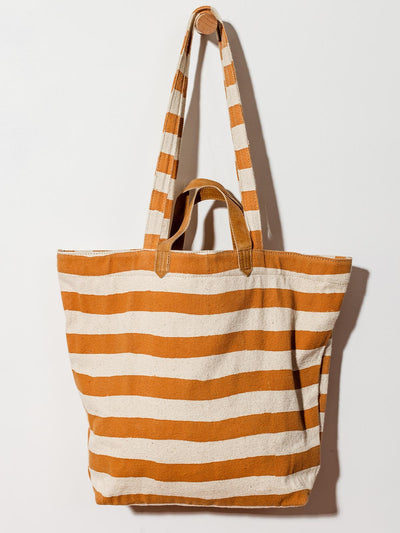 Carryall canvas tote with cream and orange stripes on white wall hanging. 