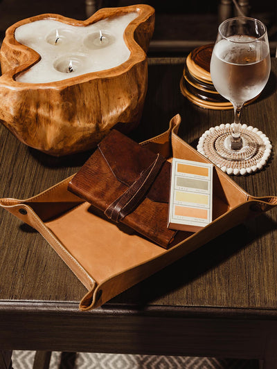 Leather large valet ray on side table in living room with candle and water glass. Tray contains a journal and box of matches 