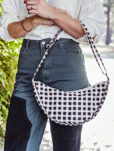 Woman modeling a black-and-white checkered crossbody bag, worn over the shoulder with an adjustable strap.