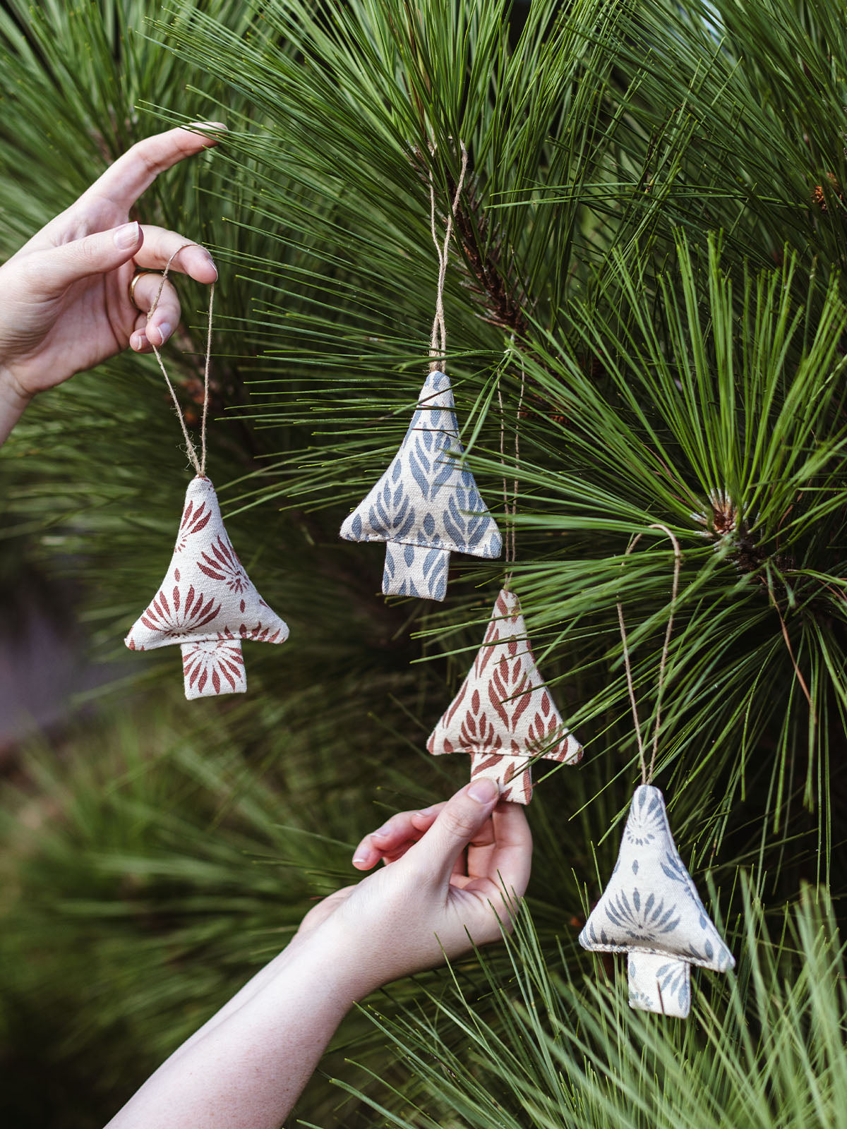 Set of four handmade fabric Christmas tree ornaments in earthy tones with block print designs, displayed on pine tree branches – sustainable holiday decor