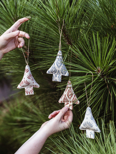 Set of four handmade fabric Christmas tree ornaments in earthy tones with block print designs, displayed on pine tree branches – sustainable holiday decor