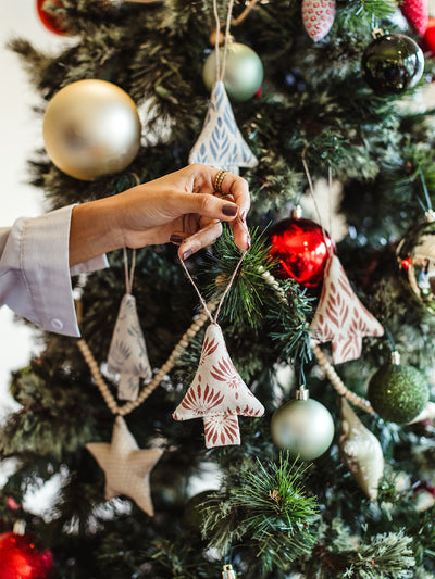Hand placing handmade fabric Christmas tree ornament with red floral pattern on a decorated Christmas tree with baubles and festive garlands.