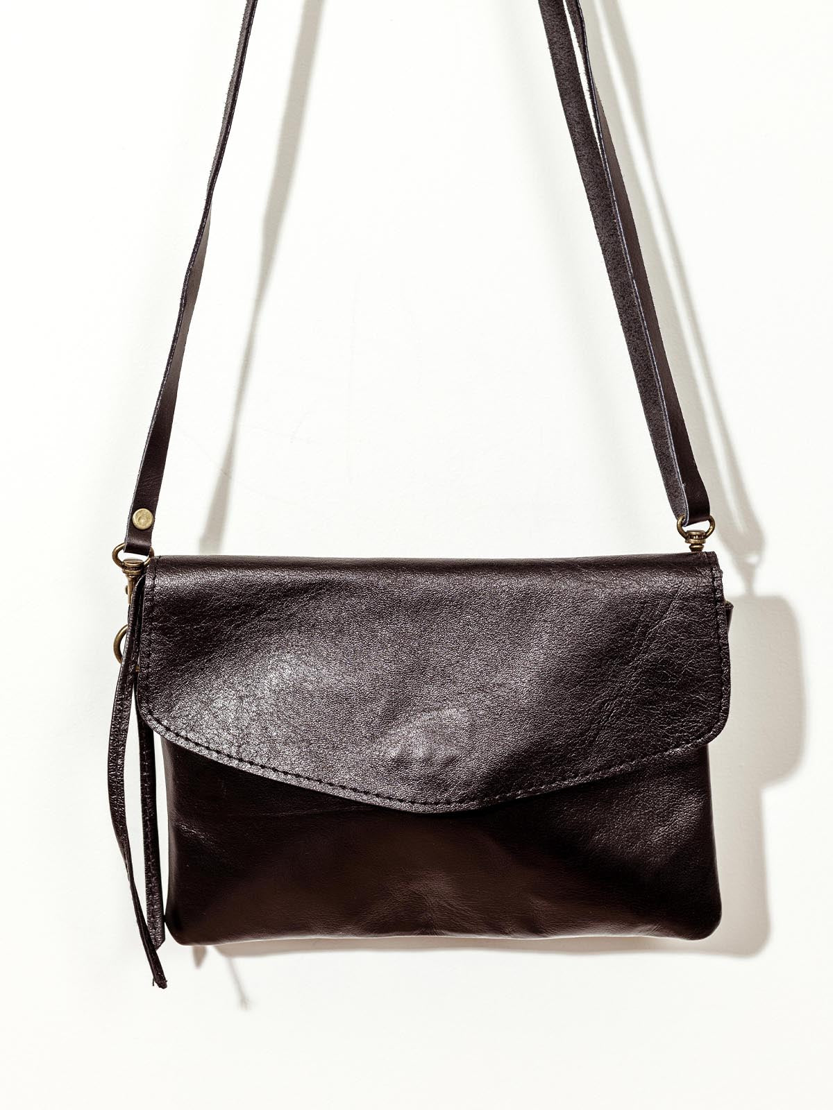 Close up of black leather crossbody clutch on white wall.