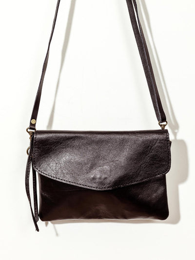 Close up of black leather crossbody clutch on white wall.