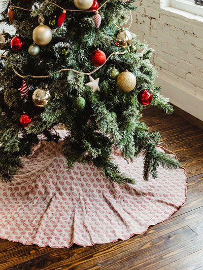 Full Christmas tree with red and gold baubles and handmade wooden bead garland, featuring a red and cream patterned block print tree skirt — ethically crafted festive home styling.