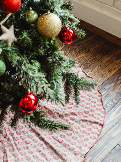 Close-up of red and cream block printed Christmas tree skirt under a decorated tree with red and gold ornaments — handmade fair trade holiday decoration.