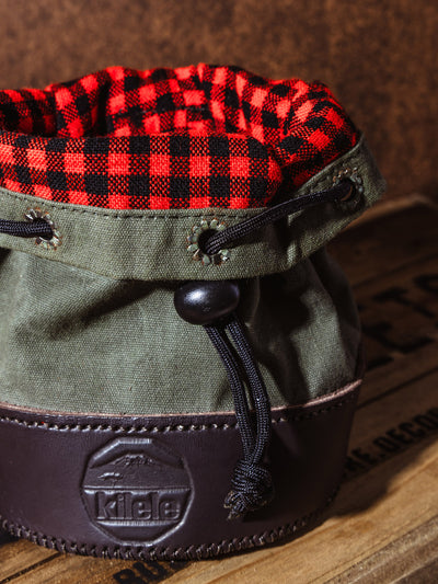 Close-up of the interior flannel lining inside the Kilele shell bag, showing red and black checkered fabric paired with olive canvas and a leather base.