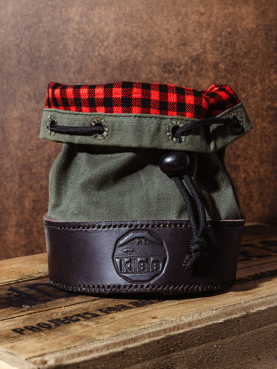 Kilele canvas and leather shell bag with red and black buffalo plaid flannel lining, photographed upright on a rustic wood crate.