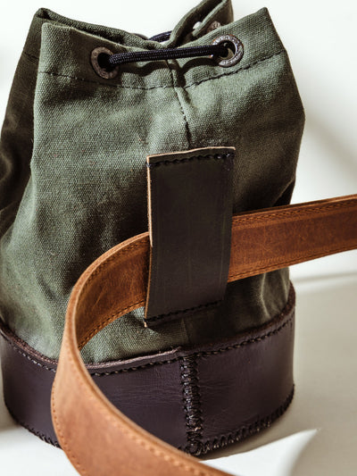 Close-up of the back of the olive canvas shell bag by Kilele, highlighting the leather belt loop with a brown leather belt threaded through for secure attachment.