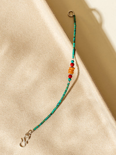 Handcrafted bracelet featuring turquoise-green beads and vibrant orange and red accents, styled on a warm beige surface with natural shadows.
