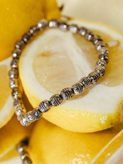 Close-up of a silver beaded bracelet with textured detailing, draped across freshly sliced lemons, creating a vibrant and zesty backdrop.