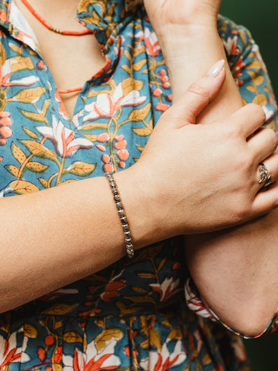 Woman wearing a silver beaded bracelet on her wrist, styled with a floral blue and orange dress and a silver statement ring, posing with hand near face.