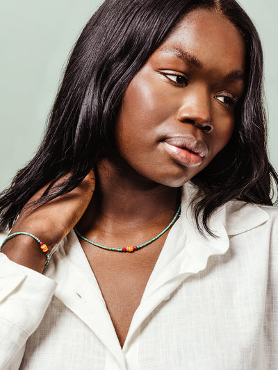 Close-up of a woman wearing a handmade beaded necklace and matching bracelet with turquoise, red, and amber-colored beads, styled with a white linen blouse.