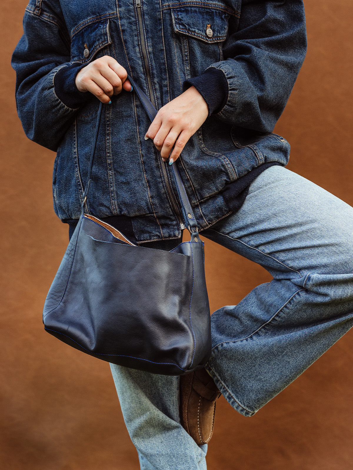 Woman wearing vintage denim jacket and jeans holding a black genuine leather shoulder bag, sustainable fashion accessory for everyday style.