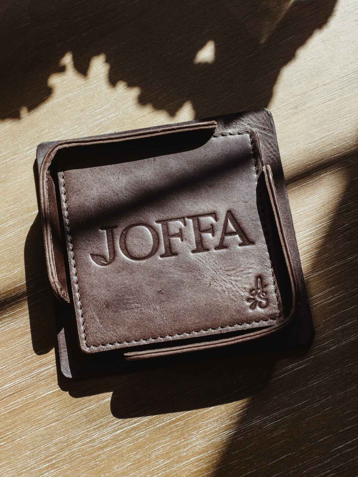 Square dark brown leather coaster set on wood table.
