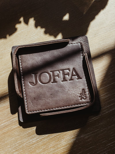 Square dark brown leather coaster set on wood table.